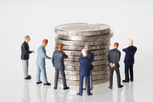 Balanță cu monede pe un taler și o plantă mică pe celălalt, simbol al alegerii între reinvestire și economisire