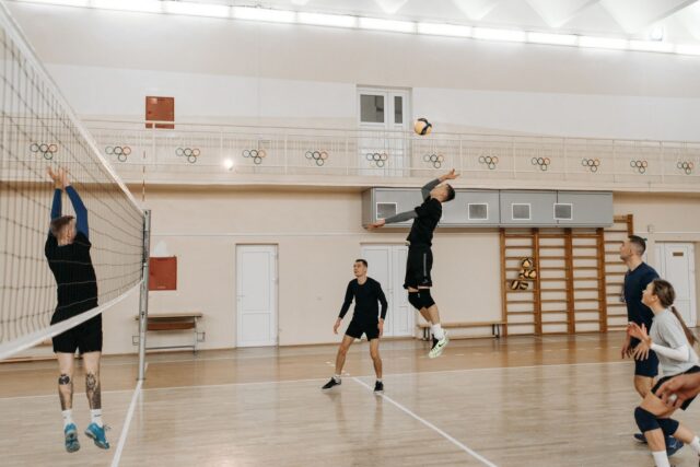 Meci amical de volei între adulți amatori într-o sală de sport, cu mingea deasupra fileului