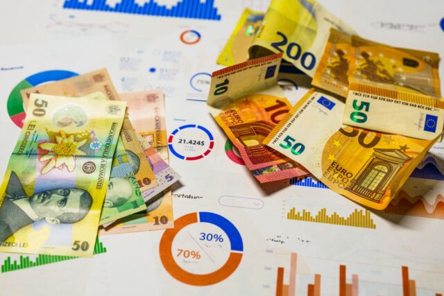 Bancnote în euro și lei așezate pe o masă, alături de un calculator și un carnet de notițe