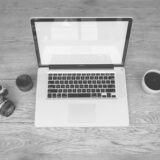 Laptop deschis, un caiet cu schițe de plan de afaceri și o cană de cafea pe un birou de acasă