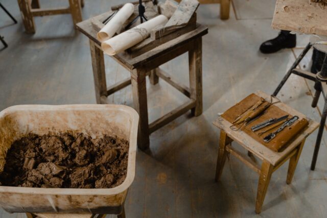 Obiecte de ceramică lucrate manual așezate pe un banc de lucru din lemn, într-un atelier mic de acasă